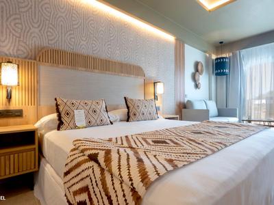 Camera d'hotel moderna con letto grande, cuscini decorativi e luce naturale.