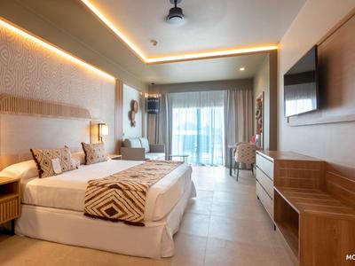 Camera d'hotel luminosa con letto matrimoniale, TV, balcone e arredamento moderno.