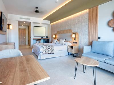 Camera d'hotel moderna con letto matrimoniale, divano, tavolo in legno e illuminazione elegante.