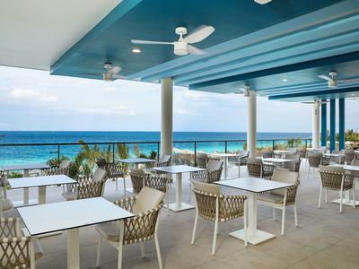 Espace repas ouvert avec tables et chaises blanches donnant sur la mer bleue.