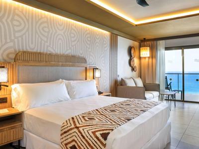 Chambre d'hôtel moderne avec lit double, canapé et terrasse avec vue sur la mer.