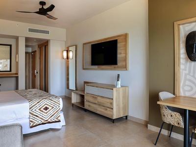 Chambre d'hôtel moderne avec deux lits, télé murale et bureau avec chaise.