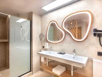 Bagno d'hotel moderno con due lavandini, specchi dalle forme organiche e arredamento beige.
