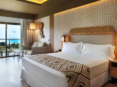 Chambre d'hôtel moderne avec grand lit, fauteuil et balcon avec vue sur la mer.