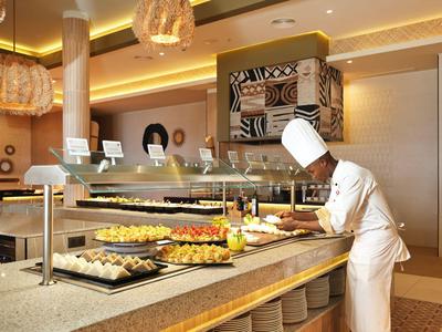 Chef en uniforme blanche préparant des plats au buffet dans un restaurant moderne.