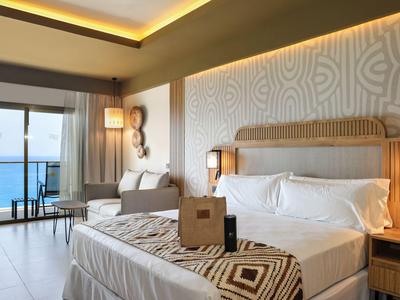 Chambre d'hôtel moderne avec lit double, canapé et balcon avec vue sur la mer.