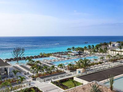 Piscina moderna dell'hotel con sdraio e vista sul mare blu sotto un cielo limpido.