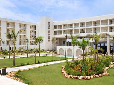 Hôtel moderne avec jardin soigné et palmiers sous un ciel bleu.