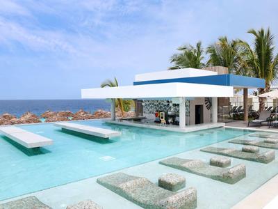 Piscina moderna con bar, lettini integrati e vista mare sotto cielo azzurro.