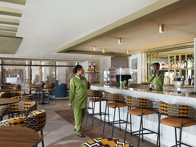 Ein moderner Hotelbarbereich mit Theke, Hockern und Gästen in grüner Kleidung.