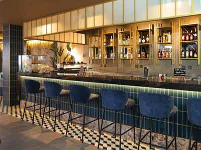 Area bar moderna dell'hotel con sgabelli blu e bancone illuminato in un ambiente elegante.