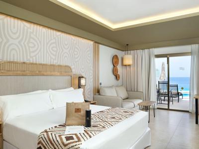 Camera d'hotel luminosa con letto matrimoniale, zona salotto e terrazza con vista mare.