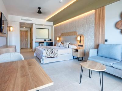 Camera d'hotel moderna con letto matrimoniale, divano, scrivania e accenti in legno caldo.