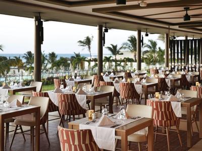 Restaurant ouvert avec tables dressées offrant une vue sur la plage et la mer.