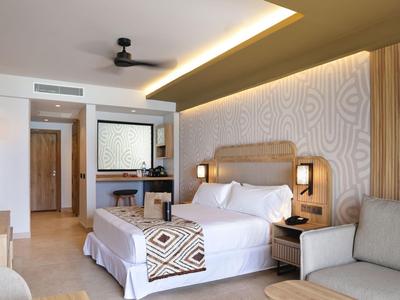 Chambre d'hôtel moderne avec lit double, coin salon et penderie ouverte dans un design lumineux.