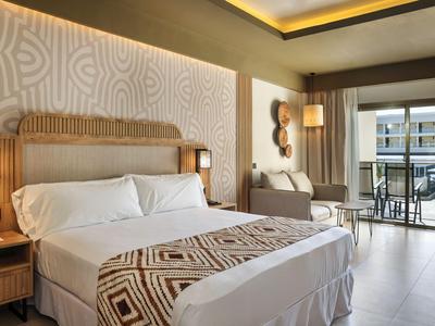 Chambre d'hôtel moderne avec grand lit, fauteuil confortable et balcon avec vue sur la ville.