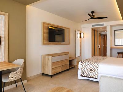 Chambre d'hôtel moderne avec lit, télévision, bureau et éclairage chaud.