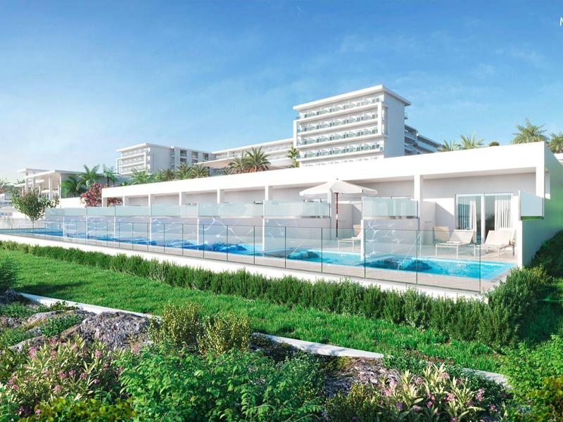 Nowoczesny hotel z tarasem przy basenie i przyległym zielonym terenem pod niebieskim niebem.