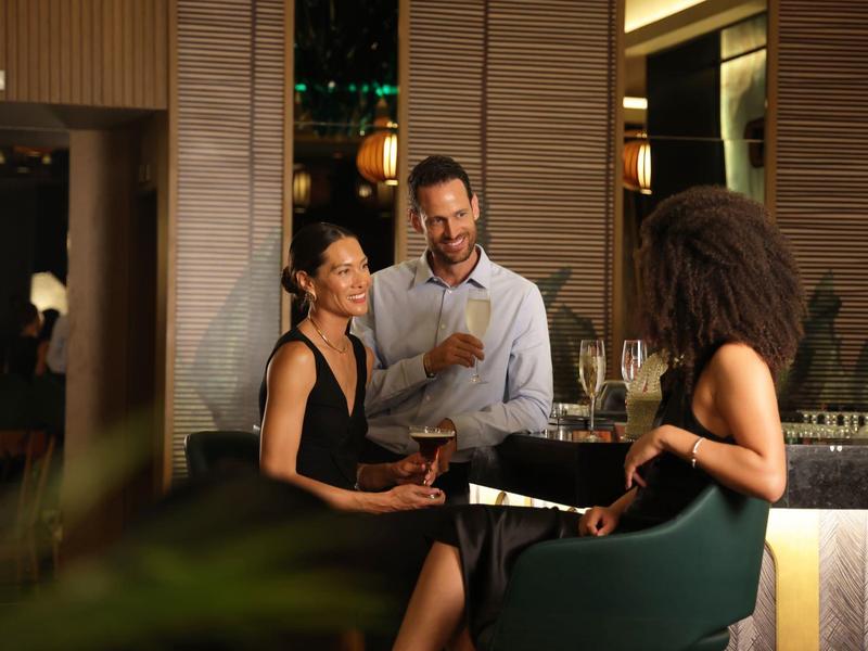Trzy osoby rozmawiają swobodnie przy barze hotelowym w stylowym otoczeniu.