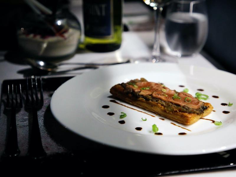 Eleganckie danie z prostokątnym kawałkiem mięsa na białym talerzu ozdobione kroplami sosu i ziołami.