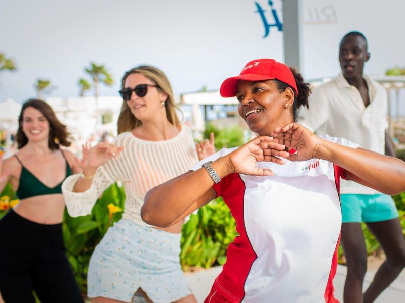 Kilka osób tańczy na zewnątrz w codziennych ubraniach przy słonecznej pogodzie.