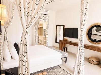 Jasny pokój hotelowy z podwójnym łóżkiem, eleganckimi zasłonami i nowoczesnym telewizorem.