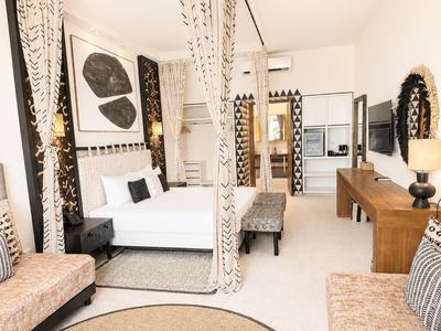 Nowoczesny pokój hotelowy z łóżkiem podwójnym, częścią wypoczynkową i drewnianymi meblami w neutralnych kolorach.