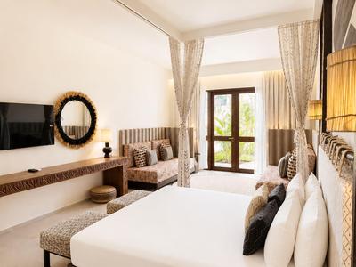 Jasny pokój hotelowy z dużym łóżkiem, sofą, lustrem i dostępem do balkonu.