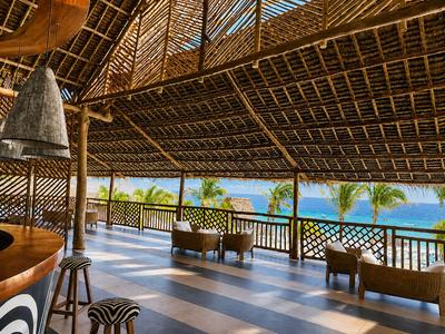 Otwarty taras z widokiem na ocean, drewniane meble i dach z liści palmowych w tropikalnym hotelu.