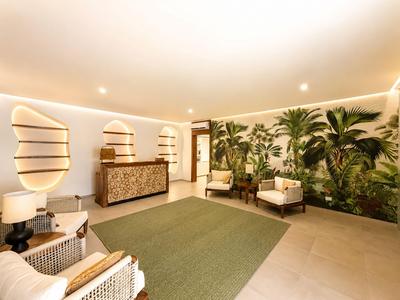 Jasna lobby hotelowa z zieloną ścianą, miejscem do siedzenia i recepcją.
