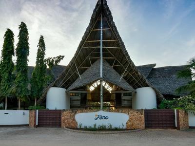 Ingang van een tropisch hotel met poort, planten en een hoog puntig dak onder een bewolkte lucht