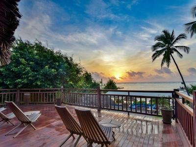 Houten terras met ligstoelen met uitzicht op zee en zonsondergang met palmbomen.
