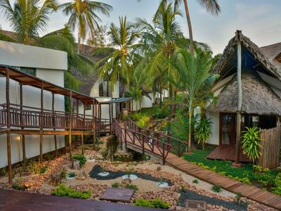 Tropisch hotel met bungalows en palmbomen verbonden door houten paden in het groen.