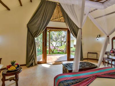 Helles Hotelzimmer mit Moskitonetzbett, Vorhängen und Zugang zu einer Terrasse mit Gartenblick.