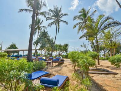 Hotelgarten mit Liegestühlen unter Palmen und Blick auf das Meer bei sonnigem Wetter.