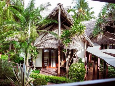 Bungalow mit Strohdach umgeben von tropischen Pflanzen und Palmen