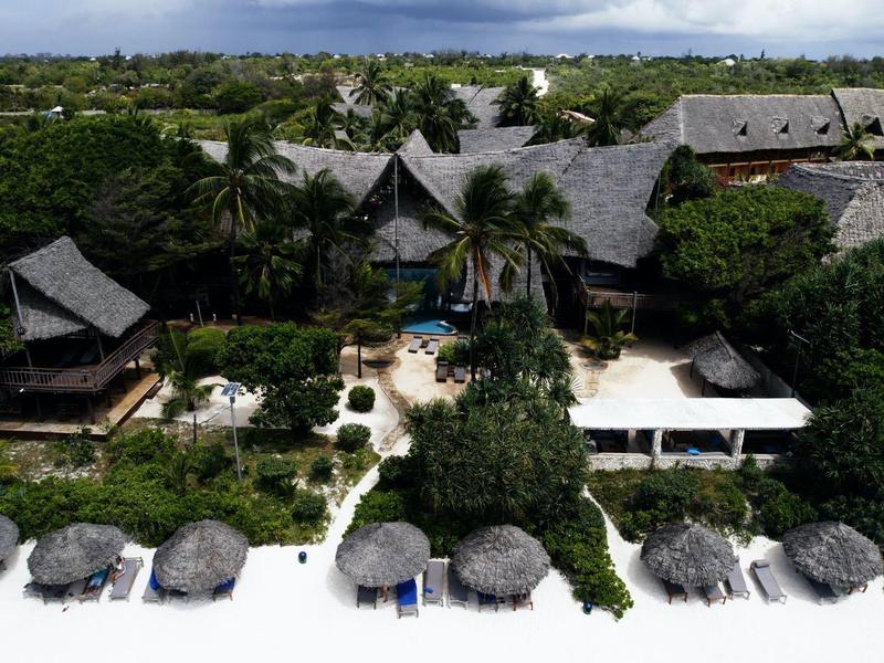 Tropisches Resort mit strohgedeckten Hütten am weißen Sandstrand und üppiger Vegetation.