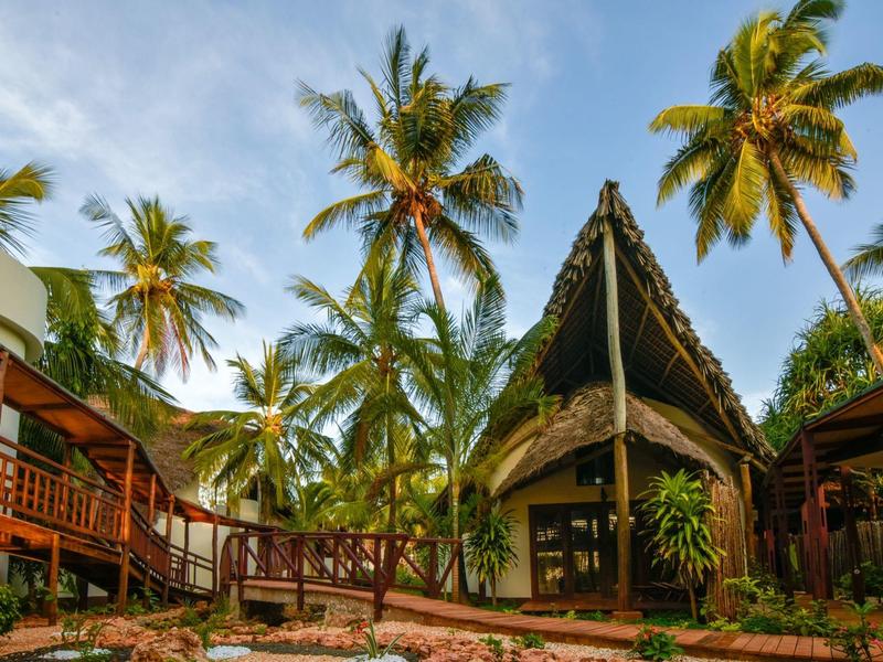 Tropisches Hotel mit Bambushütten und Palmen unter blauem Himmel.