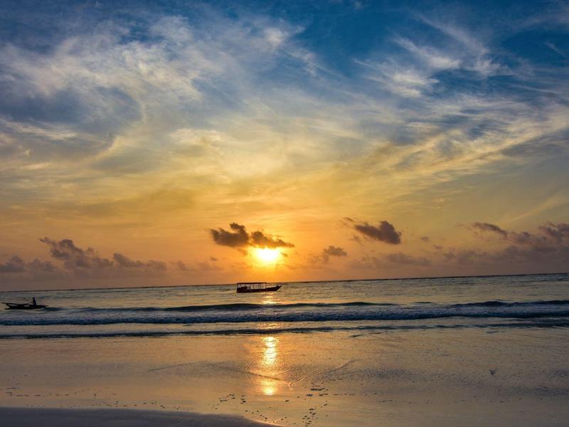 Sonnenuntergang über ruhigem Meer mit Booten und reflektierendem Sandstrand