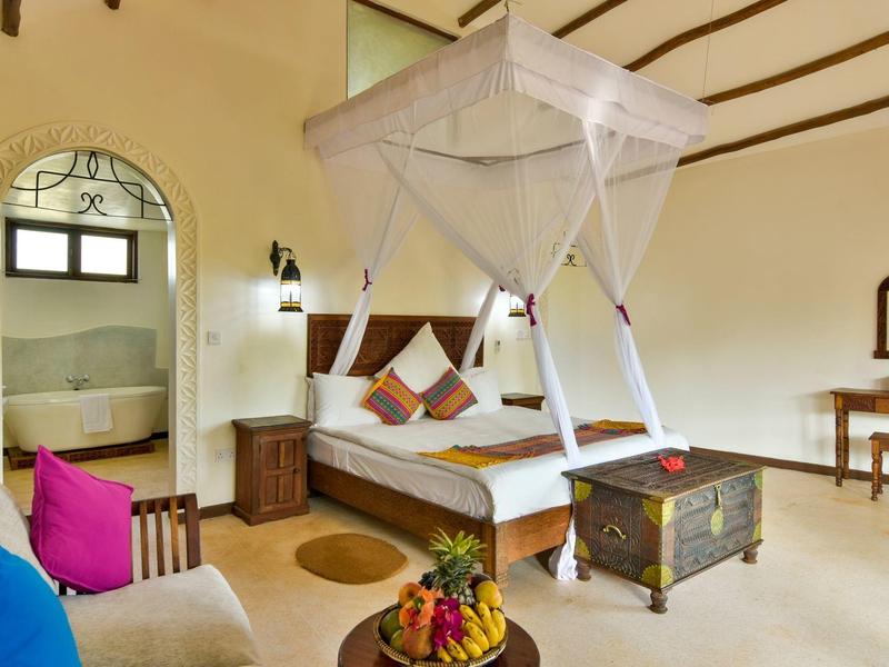 Helles Hotelzimmer mit Himmelbett, Sitzbereich und dekorativen Kissen.