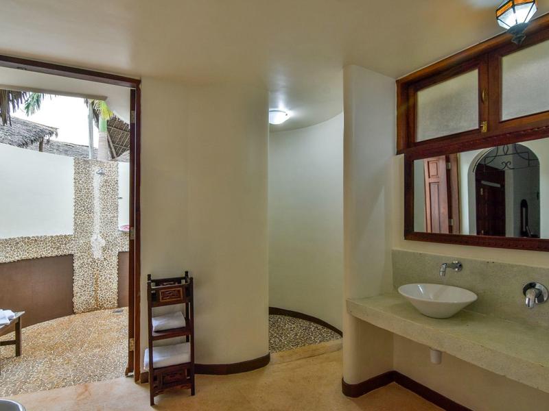 Helle Badezimmerecke mit Waschbecken, Spiegel und Zugang zu einem Außenbereich mit Dusche.