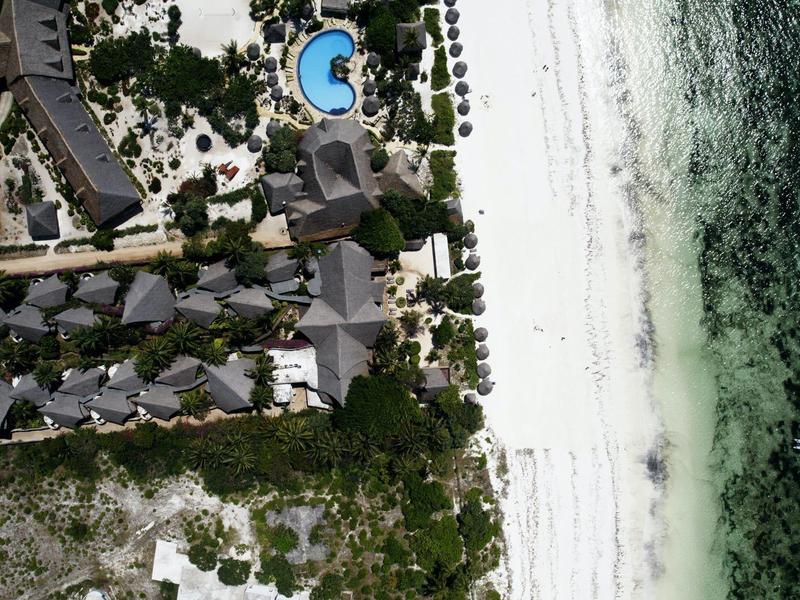 Luftaufnahme eines Resorts mit Bungalows, grünem Garten und weißem Sandstrand am Meer