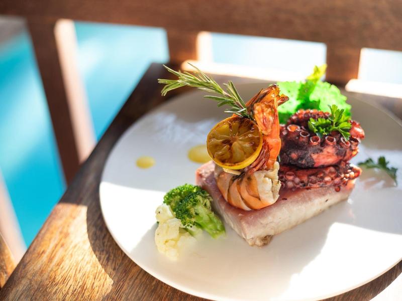 Elegantes Gourmetgericht mit Fleisch, gegrillter Zitrone und Kräutern auf weißem Teller.