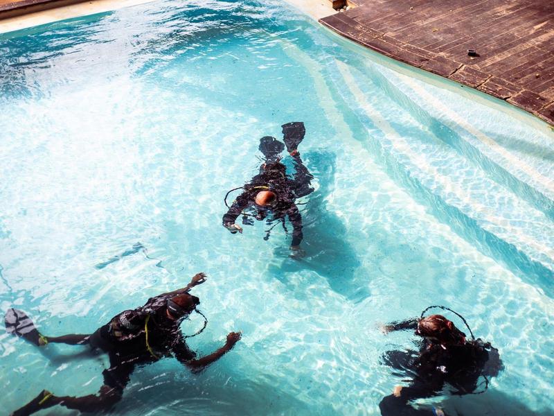 Drei Taucher üben im flachen Pool mit Tauchausrüstung und Neoprenanzügen.