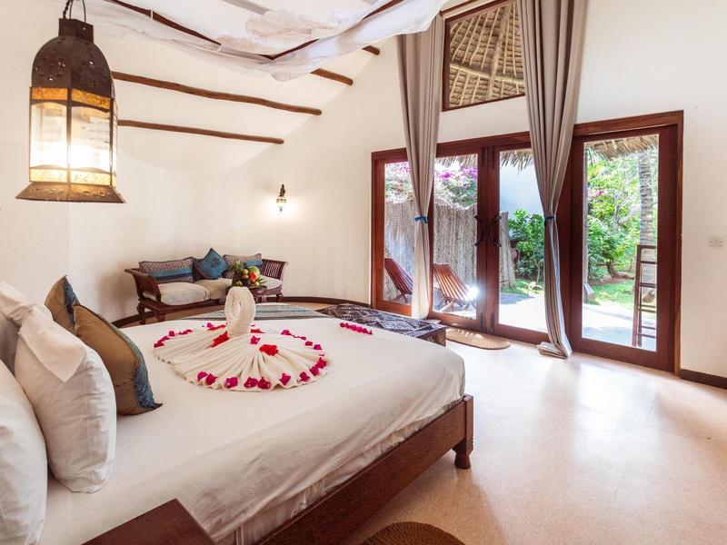 Helles Hotelzimmer mit großem Bett, gemütlicher Sitzecke und Blick auf einen Garten durch Glastüren.