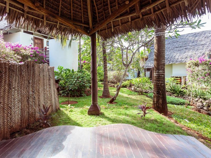 Blick von einer überdachten Terrasse auf einen tropischen Garten mit Palmen und blühenden Pflanzen