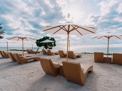 Spiaggia con ombrelloni bianchi e sedie a sdraio su sabbia chiara sotto un cielo nuvoloso.