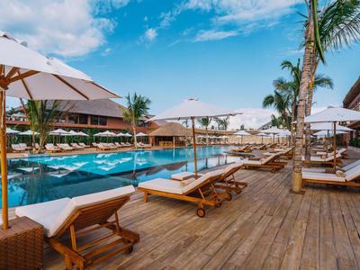 Piscina dell'hotel con lettini e ombrelloni su solarium in legno sotto cielo azzurro.