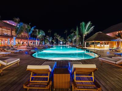 Vista notturna di una piscina d'hotel illuminata con sedie a sdraio e palme.