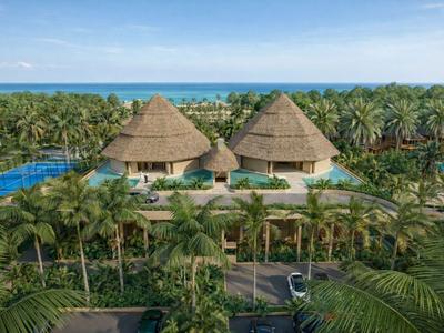 Resort tropicale con due edifici rotondi con tetto di paglia circondati da palme e vista mare.